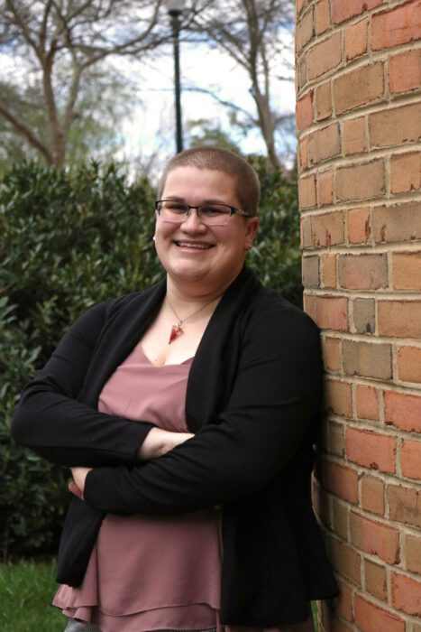 Amy Snyder smiling with her arms crossed while leaning against a brick wall.