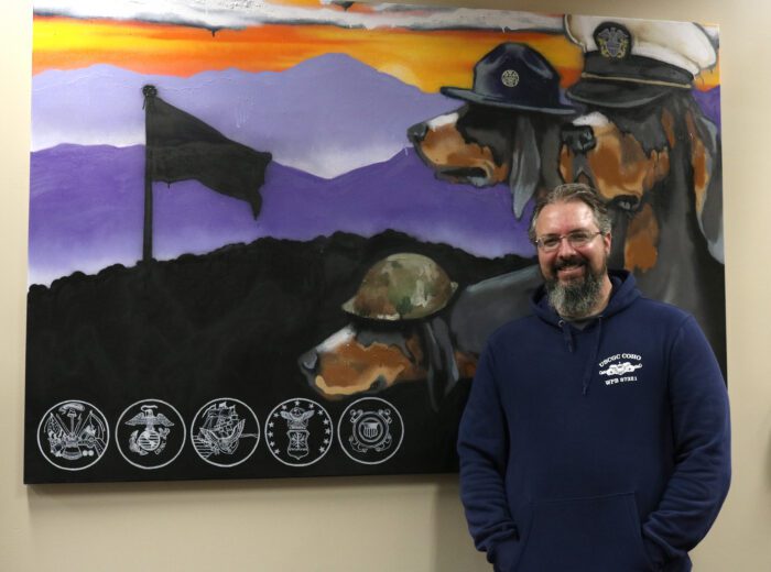 A graduate student, Chad Lanctot, stands in front of a painting of the Smokey Mountains and three Smoky dogs that hangs in the Veterans Success Center.